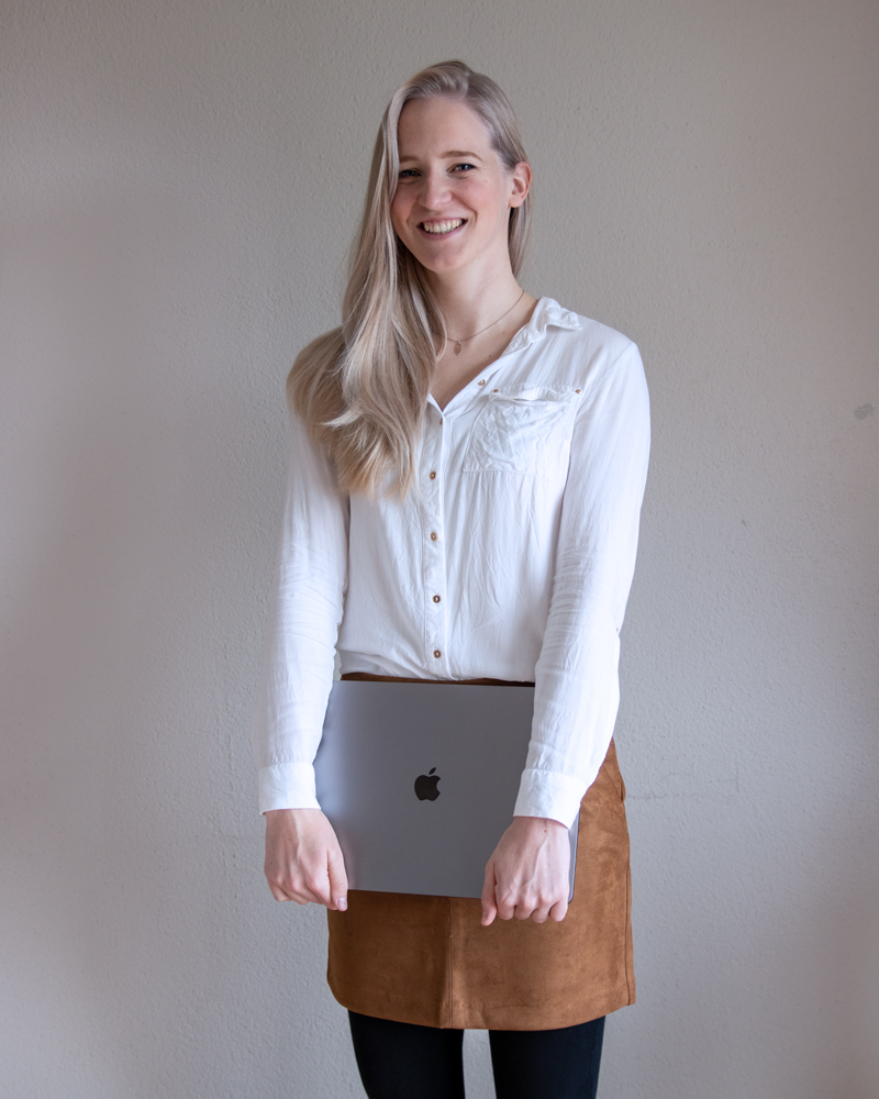 The author, Claudia, holding a laptop and smiling